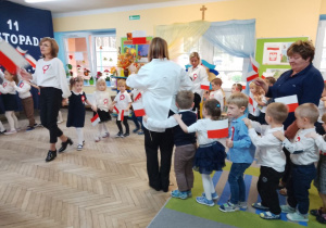 Dzieci z biało-czerwonymi flagami jadą razem z paniami w pociągach przy piosence "Jestem Polakiem".