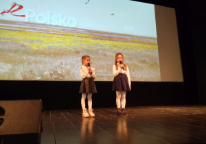 Zuzia i Julia ubrane na galowo podczas występu na scenie KDK. W tle - obraz na dużym ekranie.