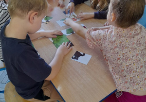 Grupka dzieci układa przy stole bajkowy obrazek z części.