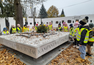 Dzieci stoją wokół płyty upamiętniającej Żołnierzy Poległych w bitwie pod Kutnem. W tle "Mur pamięci" z tablicami pamiątkowymi.