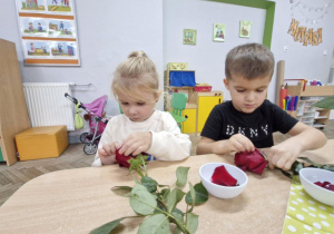 Ala i Staś siedzą przy stoliku. Dzieci trzymają w dłoniach czerwone róże.