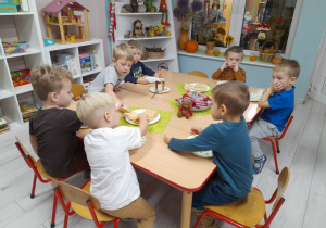 Dzieci siedzą przy wspólnym stole, na którym leżą wafelki, batoniki i miodek.