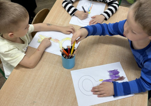 Dzieci wykonują pracę plastyczną przy stoliczkach.