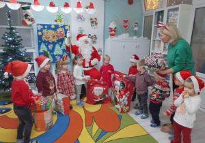 Dzieci z panią Grażynką odbierają prezenty. Dzieci stoją w półkolu i trzymają prezenty.