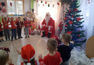 ”Biedronki” stoją w półkolu i prezentują piosenkę dla Mikołaja.