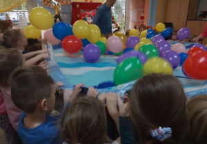 Dzieci trzymają chustę, na której są kolorowe balony.