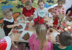 Dziewczynki ozdabiają czekoladowe choinki słodkimi dodatkami.