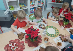 Dziewczynka i trzech chłopców dekoruje swoją czekoladową choinkę groszkami, rodzynkami, wiórkami i innymi smakołykami.