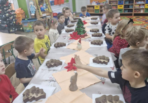 Dzieci siedzą wspólnie przy świątecznie udekorowanym stole; przed przedszkolakami leżą foremki w kształcie choinek.