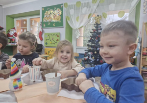 Majka, Zuzia i Tymuś siedzą przy stole, na którym widać choinkowe foremki i kubeczki pełne czekolady.