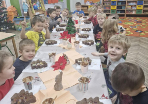 Przedszkolaki siedzą przy stole i ozdabiają posypkami swoje czekoladowe choinki.