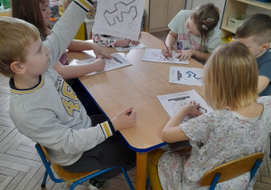 Grupka dzieci przy stoliku wypełnia karty pracy "Poprowadź szczoteczkę z pastą do Mleczaka".