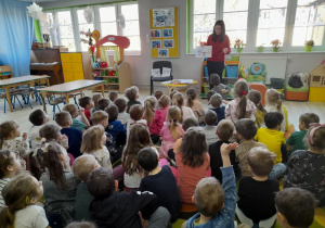 Dzieci siedzą na dywanie, a Pani doktor pokazuje planszę z akcesoriami do higieny jamy ustnej.