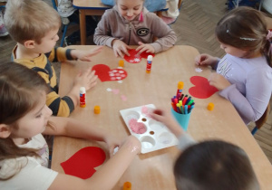 Dzieci przy stolikach wyklejają kwiatkami Walentynkowe serca.