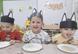 Szymek, Franuś i Staś siedzą przy stoliku. Przed chłopcami ustawione są spodeczki z mleczkiem.