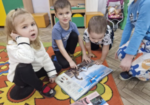 Dzieci siedzą na dywanie i oglądają książki o dinozaurach.