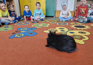 Dzieci siedzą na dywanie, po którym skacze maleńki króliczek.