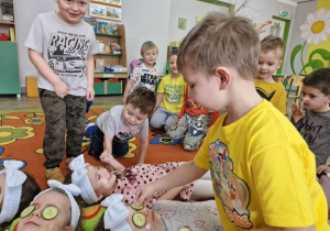 Tymuś nakłada plasterki ogórka na powieki Mai.