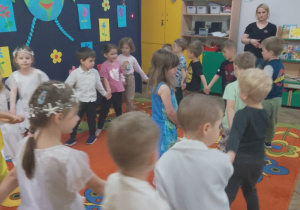 Przedszkolaki tańczą w kółeczku trzymając się za ręce. W środku kółka stoi Weronika.