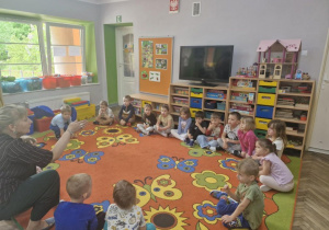 Dzieci siedzą w kółku na dywanie i z uwagą słuchają pani Ewy - przedstawiciela Biblioteki Pedagogicznej w Kutnie.