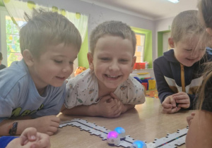 Ignaś, Franek i Julek oglądają Ozoboty poruszające się po ścieżce z ułożonych puzzli.