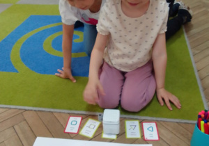 Łucja programuje GeniBota za pomocą kart. Jej działania obserwuje Matylda.