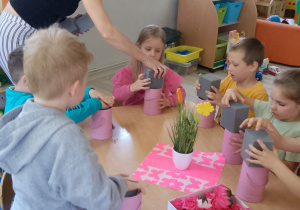 Dzieci wkładają gąbki do pudełek, a pani Kasia pomaga dziewczynce włożyć gąbkę do różowego pudełka.