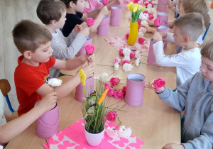 Przedszkolaki siedzą przy wspólnym stole podczas tworzenia bukietów z kwiatów mydlanych.