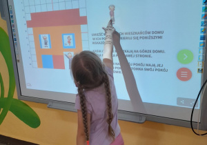 Julka przesuwa na tablicy multimedialnej obrazek przedstawiający członka rodziny według podanych wskazówek.