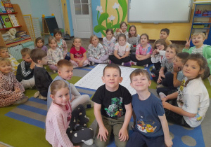 Dzieci siedzą na dywanie, a w środku leży mata do kodowania.