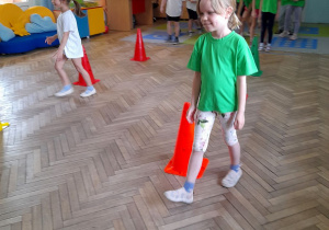 Matylda i Łucja idą między pachołkami z woreczkiem na głowie. W tle dzieci z dwóch drużyn czekają na swoją kolej.