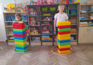 W obręczy znajdują się zbudowane przez dzieci dwie wieże z klocków. Obok stoją przedstawiciele dwóch drużyn.