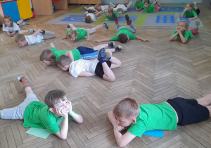 Dzieci leżą na kartkach dotykając ja brzuchami.
