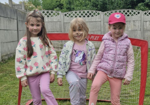 Oliwia, Nadia i Ola stoją przed bramką i stopami przytrzymują piłkę.