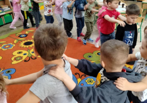 Dzieci ustawione w pociąg bawią się w sali.