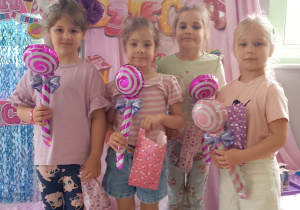 Grupka dziewczynek pozują do zdjęcia na tle dekoracji z otrzymanymi upominkami.