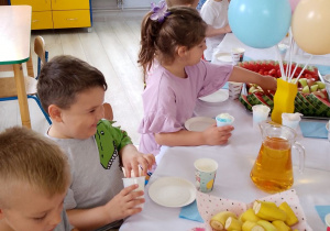 Grupka dzieci siedzi przy wspólnym stole podczas poczęstunku.