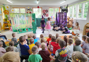 Na środku sceny odtwarzają swoje role Mikołaj w roli Żabki, Nadia w roli Wróżki i Ula w roli Małej Czarowniczki. Obok siedzą dziewczynki przebrane za Czarownice i Julka jako Narrator.