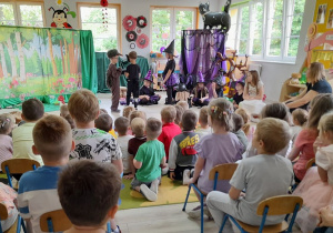 Dzieci oglądają dalszy ciąg przedstawienia. Na scenie swoje role prezentują Mikołaj jako Jeżyk, Staś jako Wilk i Ula jako Mała Czarowniczka. W tle chata Czarownic i dekoracja lasu.