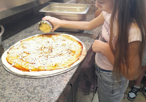 Lena posypuje pizzę serem.