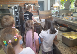 Grupka dzieci obserwuje jak Pani wałkuje ciasto na pizzę.