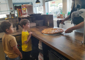 Dwóch chłopców obserwuje jak Pani kroi pizzę.