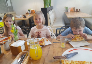 Troje dzieci siedzi przy stole podczas degustacji pizzy.