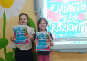 Julia i Wiktoria prezentują dyplomy zdobyte w konkursie plastycznym "Miasto róż rozkwita".