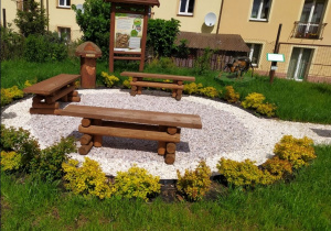 Część tematyczna "Z wizytą u mrówek": w kole wysypanym grysem stoją trzy ławki, za nimi znajduje się przyrząd interaktywny "Mrowisko", tablica dydaktyczna, rzeźba mrówki.