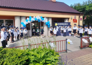 Dzieci ubrane na galowo stoją na tarasie w dwóch półkolach, a troje dzieci wyprowadza proporzec Przedszkola Miejskiego nr 5 "Stokrotka" w Kutnie.