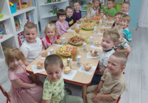 Grupa uśmiechniętych „Pszczółek” siedzi przy zastawionych smakołykami stołach.