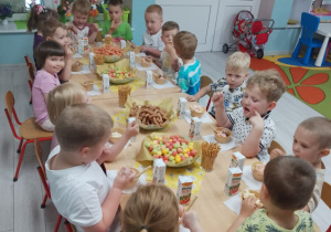 Dzieci siedzą przy stole i zajadają lody.