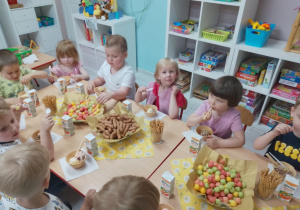 Druga część grupy przy stole na tle półek z zabawkami.