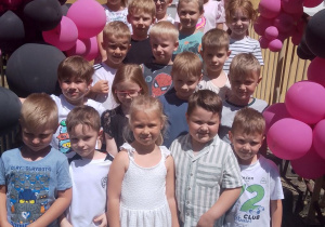 Zdjęcie grupowe dzieci na schodach przedszkola udekorowanych balonami różowo – czarnymi.